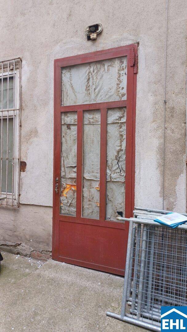 Nahaufnahme einer alten roten Tür mit abblätternder Farbe und beschädigtem Glas in einer verputzten Wand.