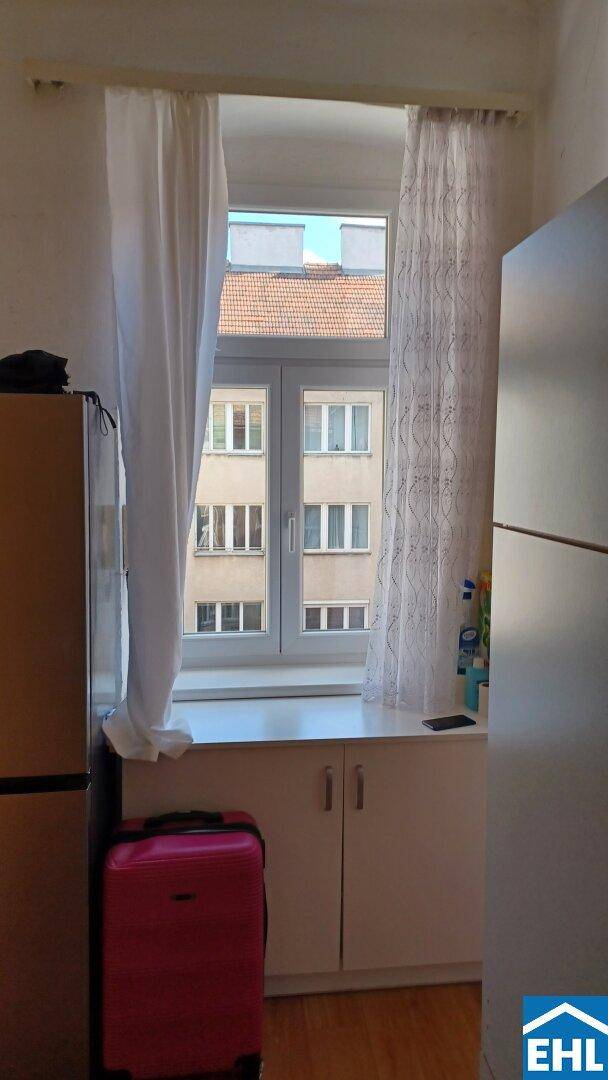 Fenster mit Blick auf gegenüberliegende Gebäude und einen roten Koffer im Vordergrund.