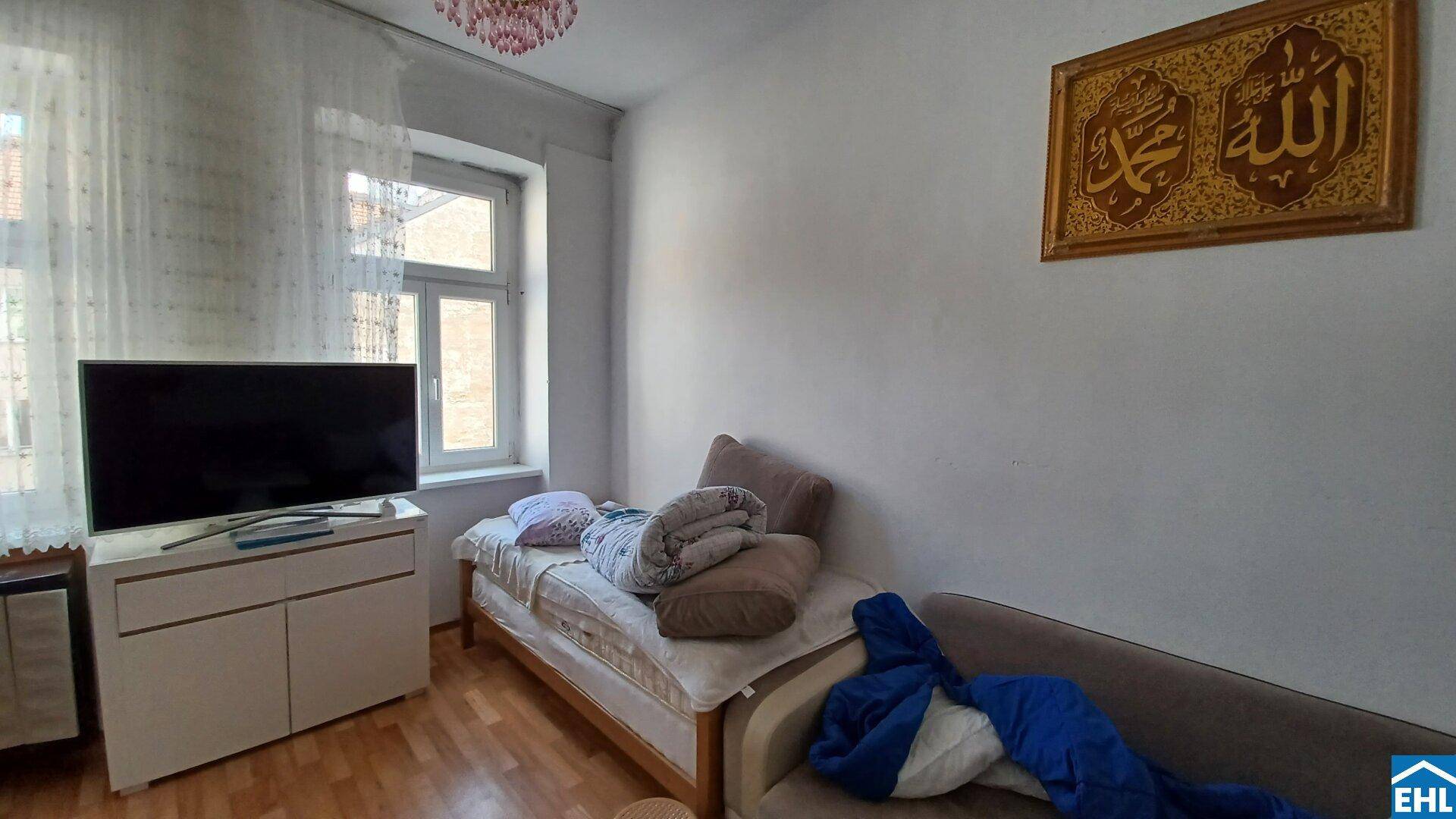 Helles Wohnzimmer mit Tagesbett, Fernseher und Fenster mit Blick nach draußen.