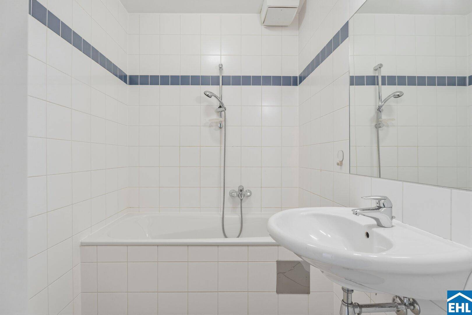 Helles Badezimmer mit Badewanne, Duschfunktion und weiß-blauen Fliesen.