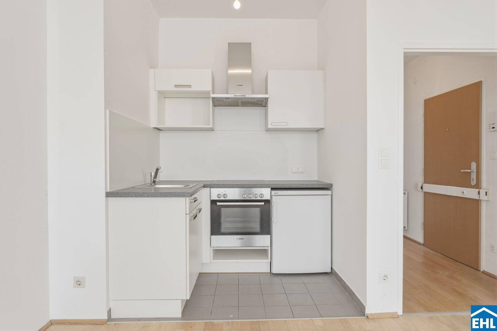 Kompakte Küchenzeile mit weißen Schränken, Spüle, Herd und Kühlschrank, funktional und platzsparend.
