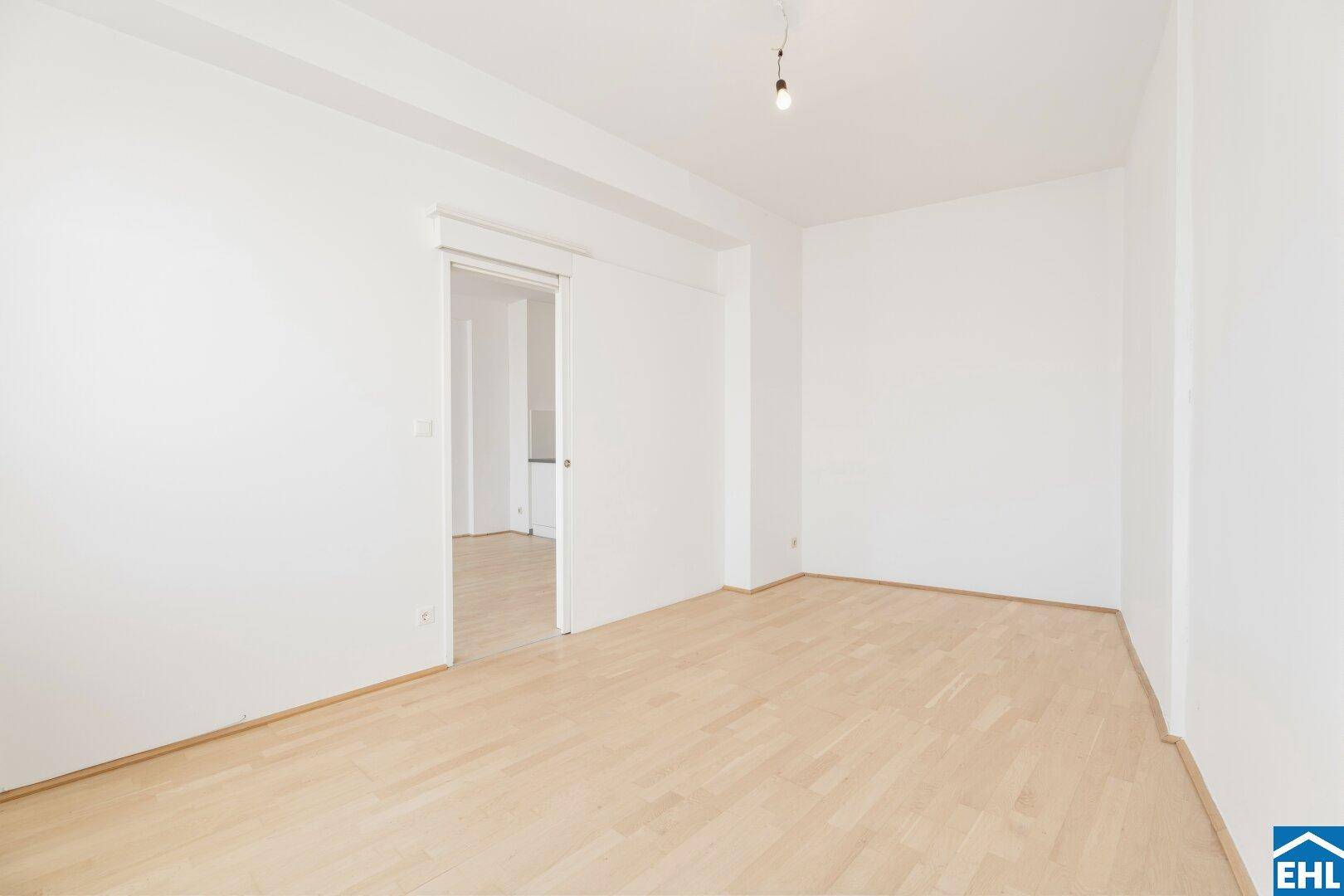 Geräumiges Schlafzimmer mit hellem Parkettboden und Schiebetür, ideal für flexible Raumgestaltung.