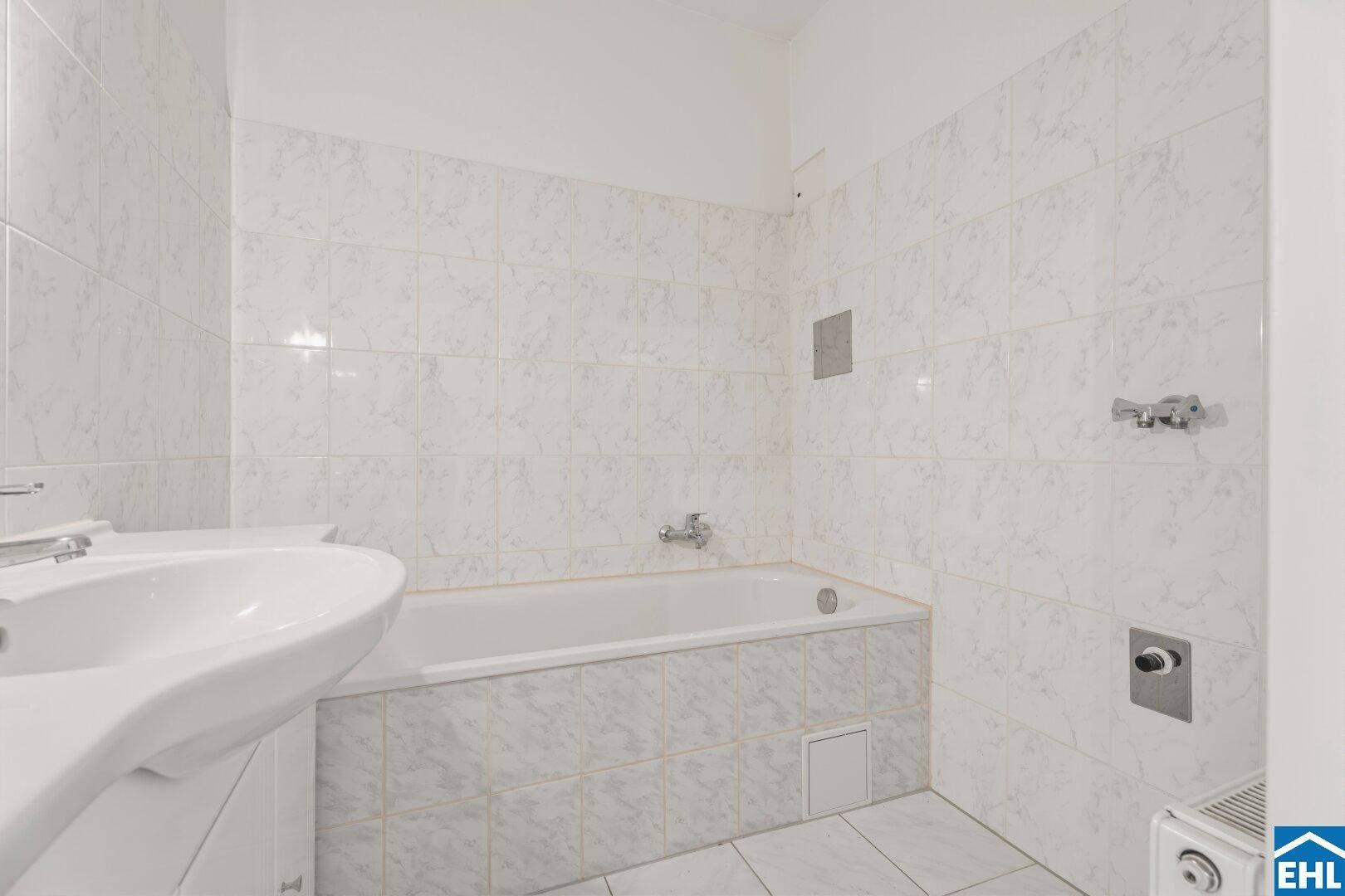 Badezimmer mit Badewanne, Waschbecken und weißen Fliesen, funktional und hell gestaltet.