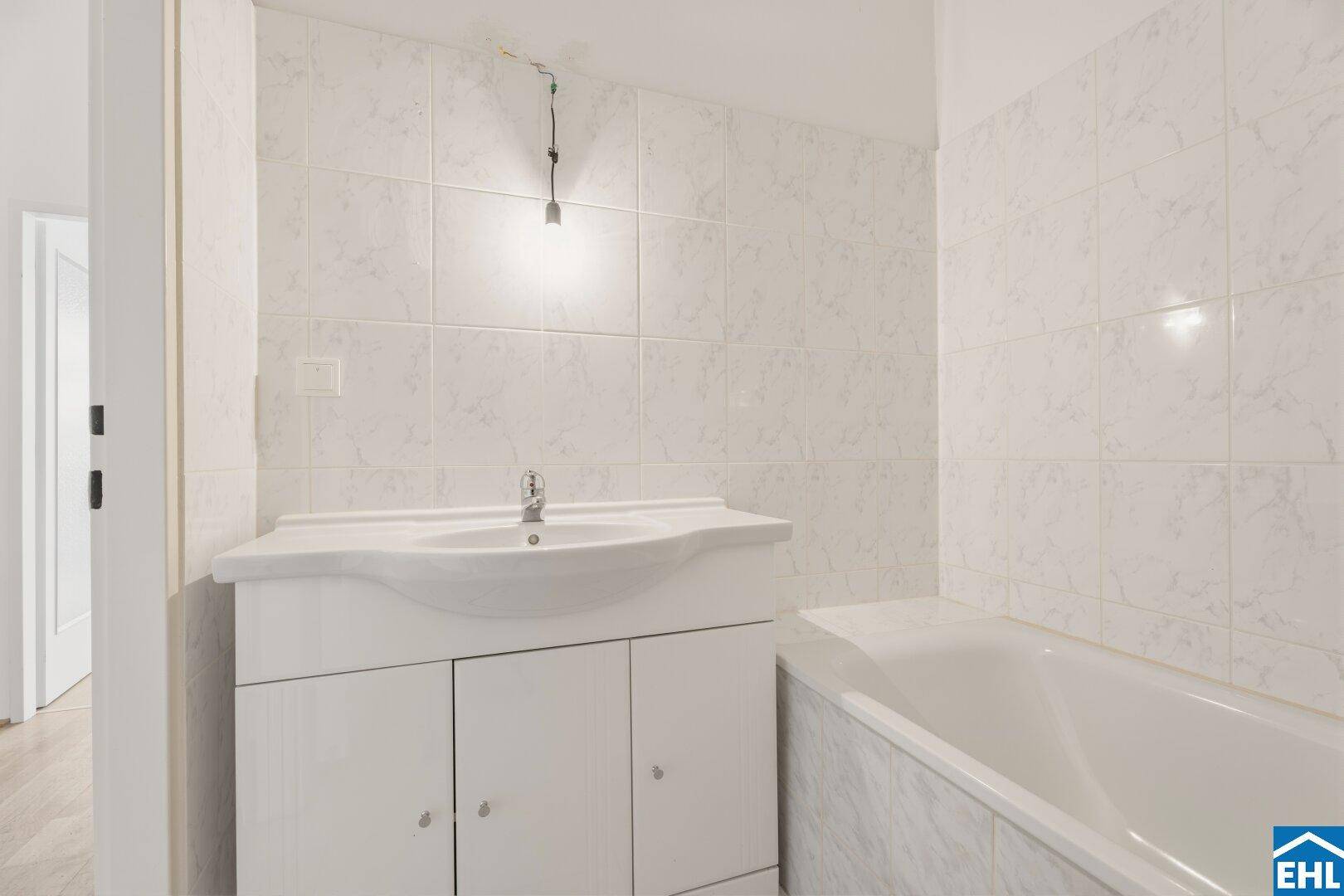 Badezimmer mit Waschbecken und Badewanne, komplett gefliest in hellem Weiß mit dezentem Muster.