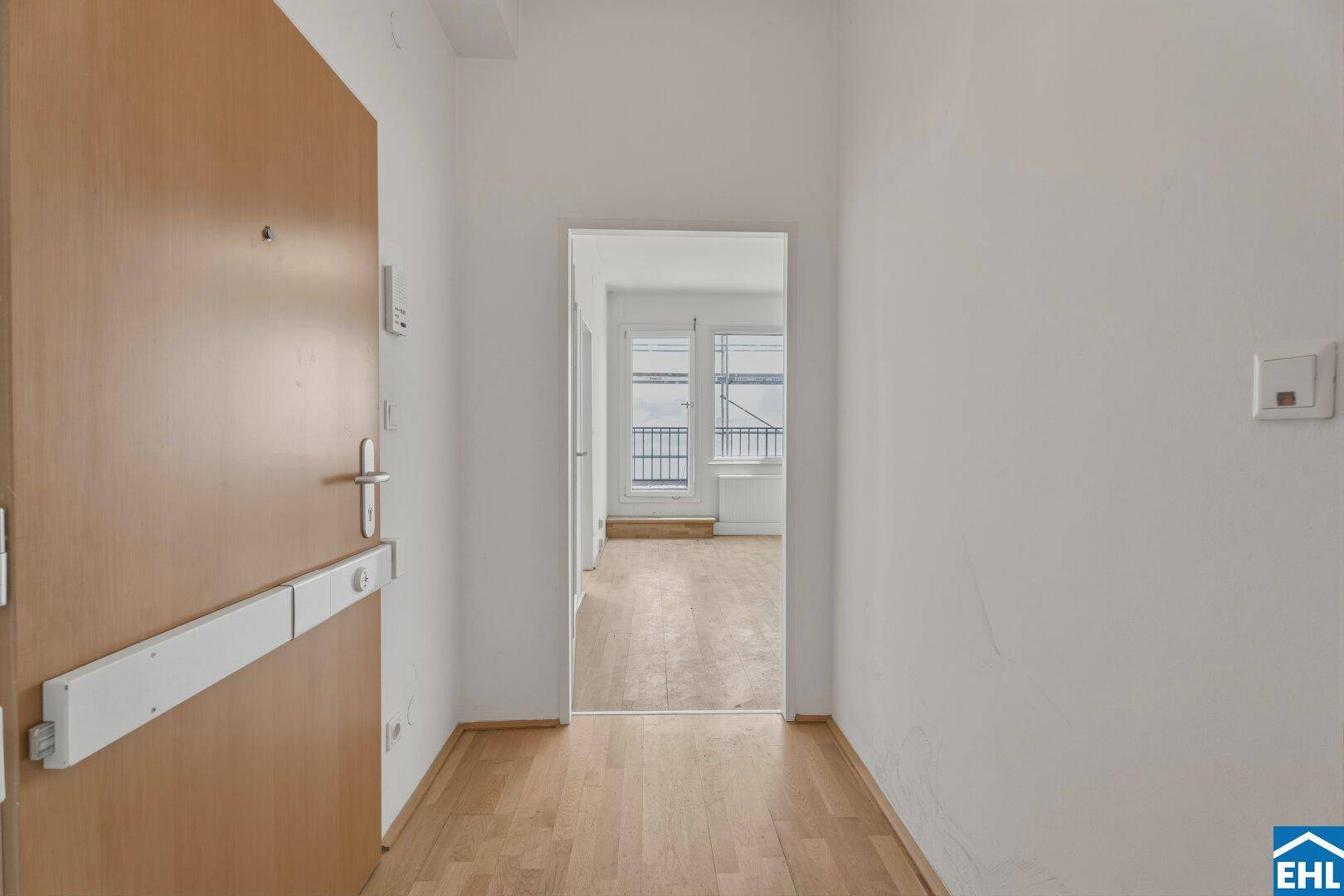 Eingangsbereich mit Holztür und hellem Parkettboden, der zu den Wohnräumen der Wohnung führt.