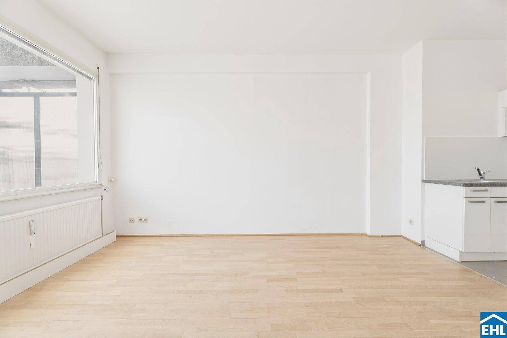 Heller Wohnbereich mit Parkettboden und großem Fenster, das viel Tageslicht spendet und den Raum erhellt.