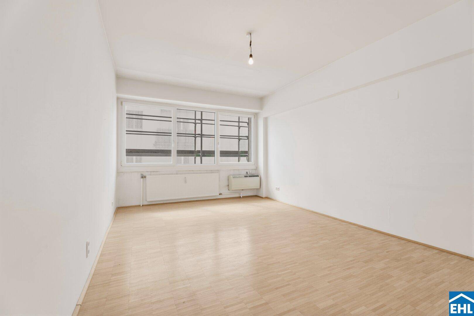 Geräumiger Wohnraum mit großen Fenstern und hellem Parkettboden, bietet viel Tageslicht und eine offene Atmosphäre.