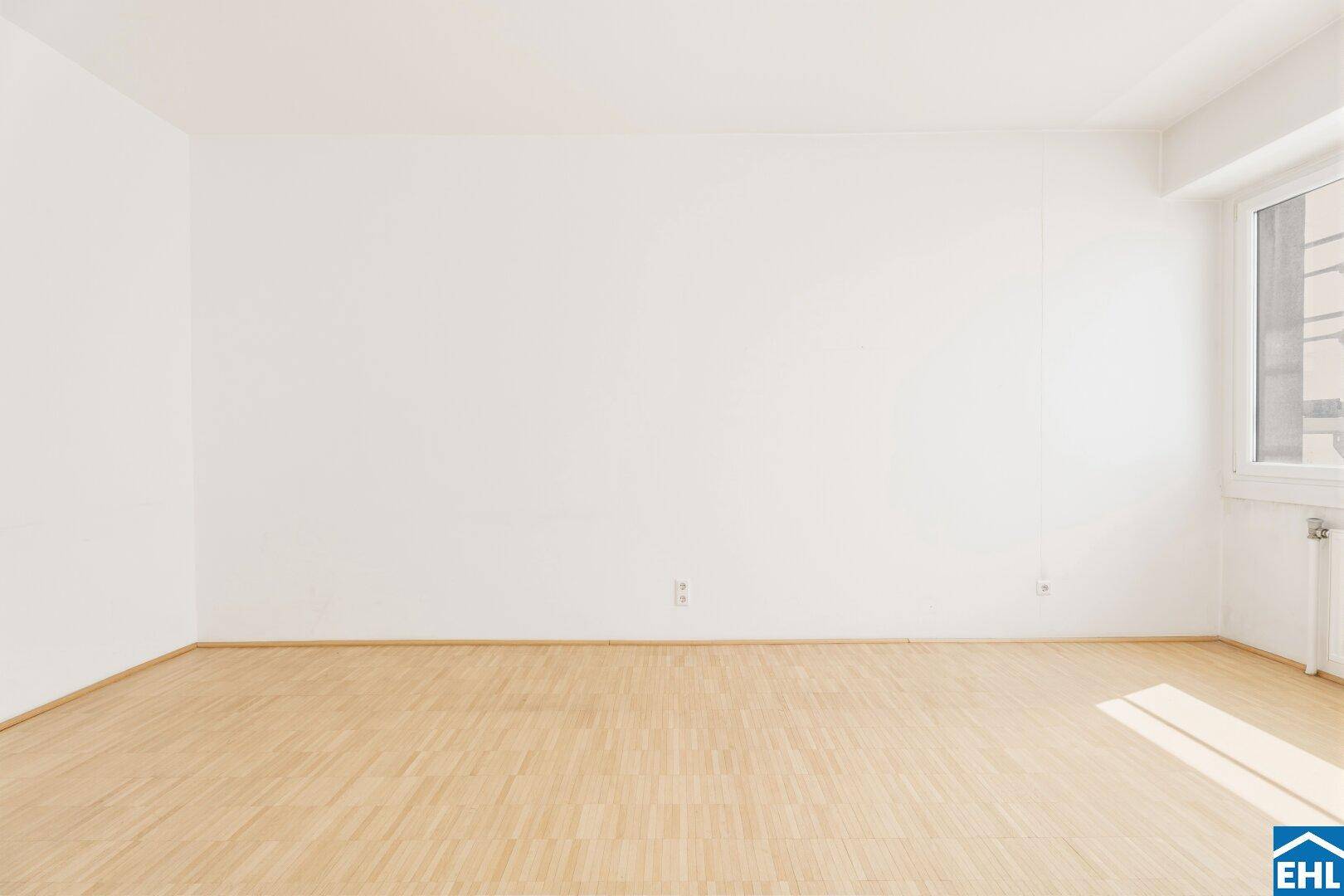Heller Wohnraum mit Fenster und Parkettboden, bietet eine angenehme Lichtsituation und viel Platz.