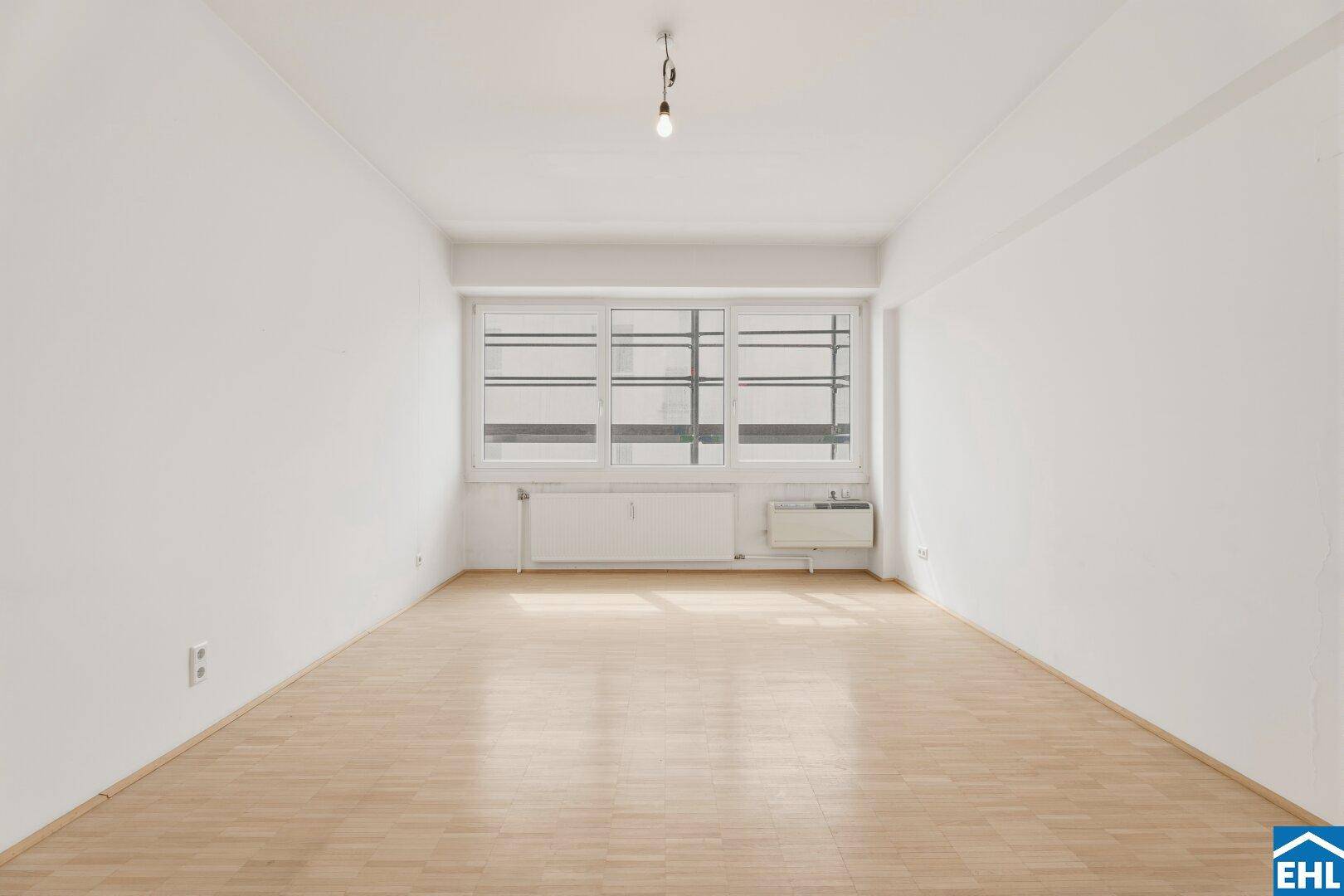 Geräumiger Wohnraum mit großen Fenstern und hellem Parkettboden, bietet viel Tageslicht und eine offene Atmosphäre.