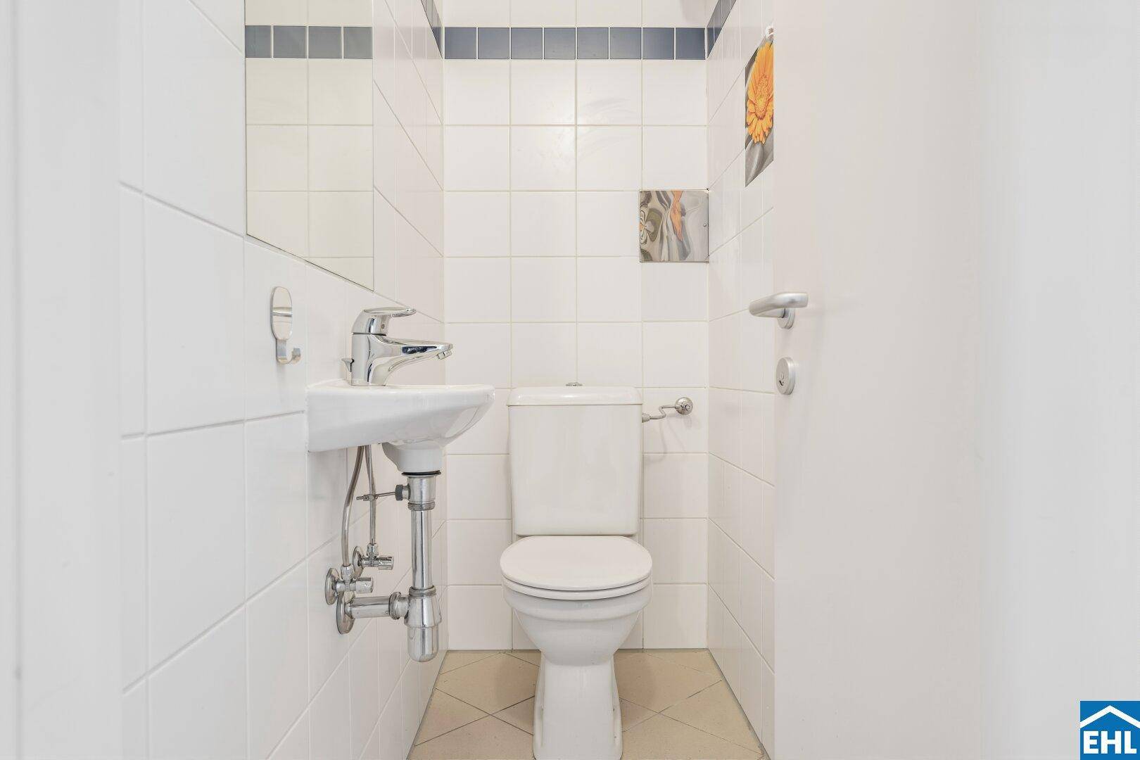 Separates WC mit kleinem Waschbecken und weißen Fliesen, bietet zusätzliche Bequemlichkeit.