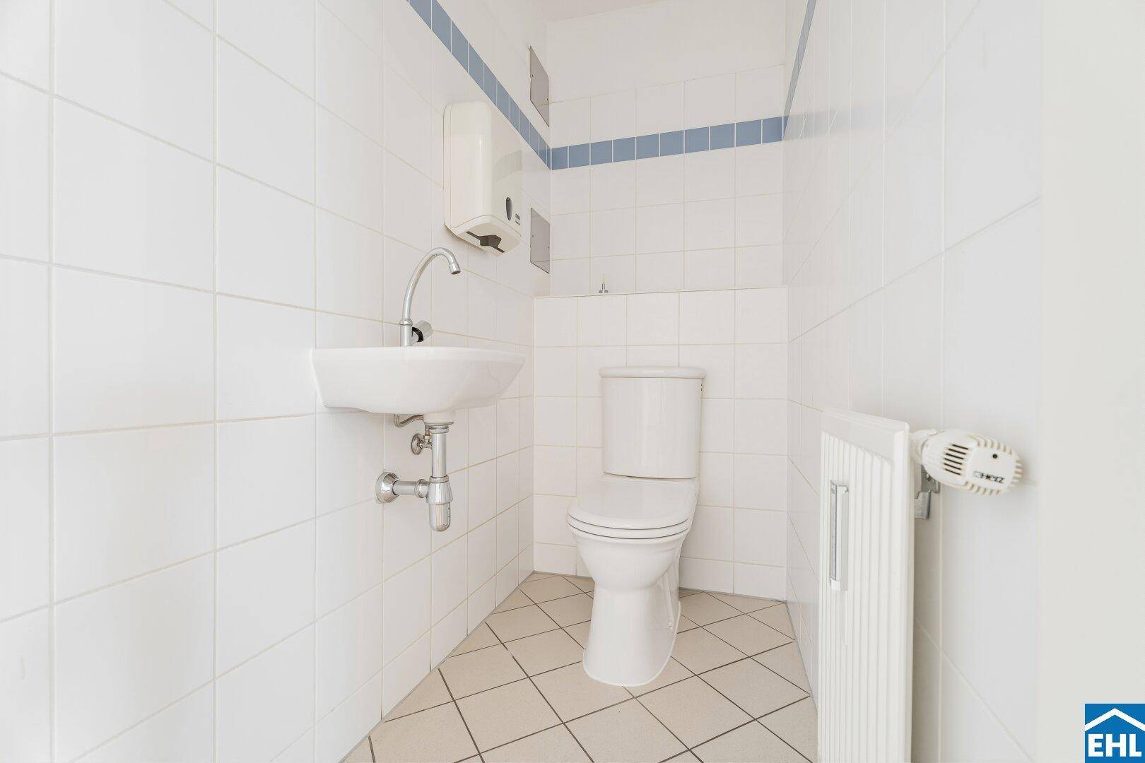 Kleines Gäste-WC mit weißen Fliesen, Waschbecken und Heizkörper.