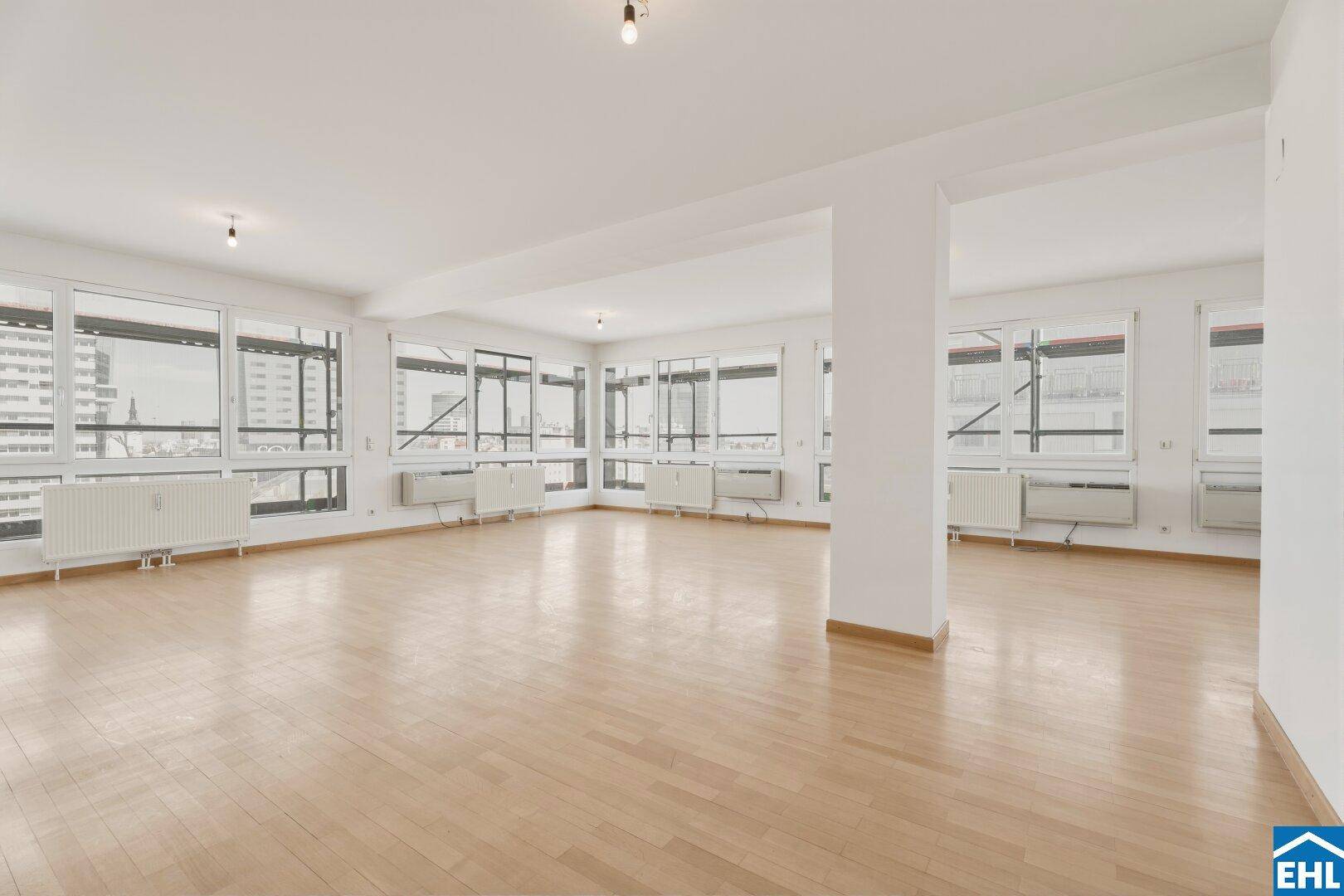 Geräumiger, heller Raum mit vielen Fenstern und Parkettboden, ideal für offenes Wohnen.