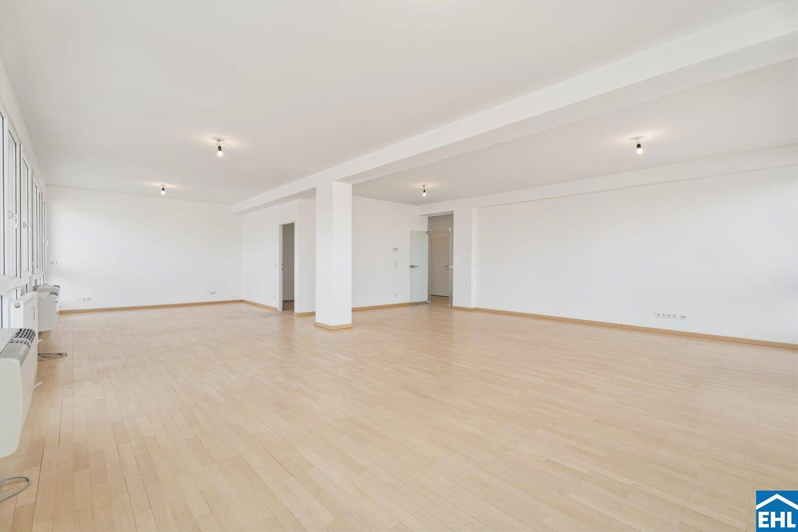 Weitläufiger Raum mit Parkettboden, weißen Wänden und viel Tageslicht.