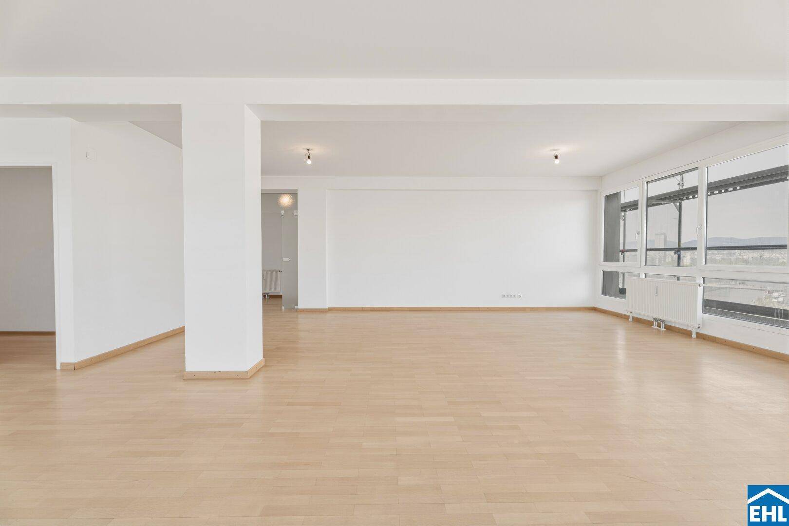 Heller Wohnbereich mit Parkettboden und einer langen Fensterfront.