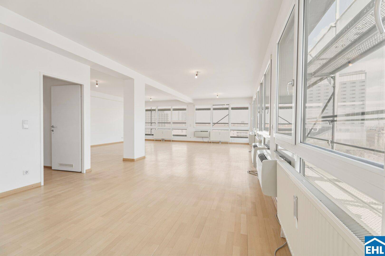 Geräumiger Raum mit Parkettboden und durchgehender Fensterfront.