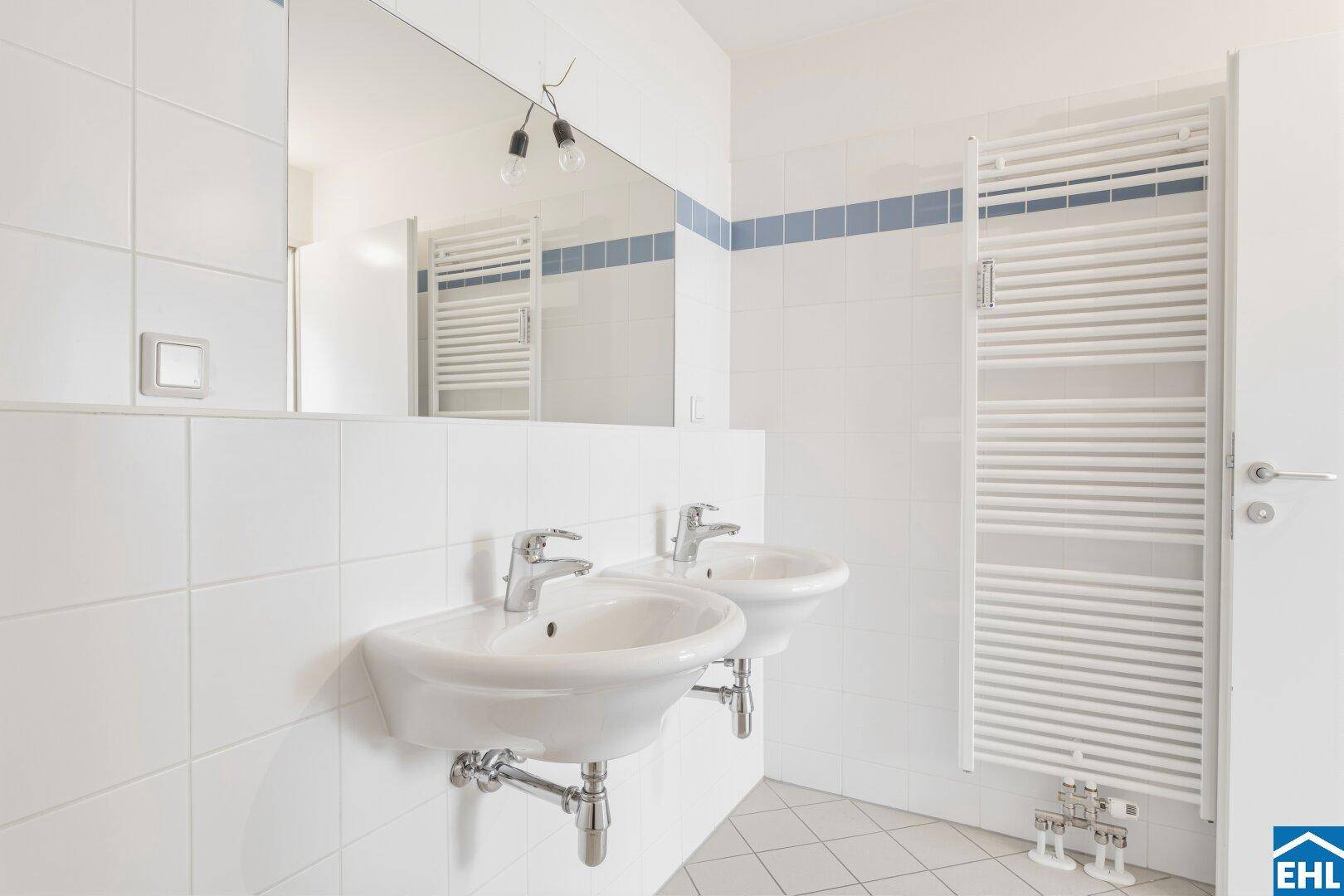 Helles Badezimmer mit Doppelwaschbecken, Spiegel und Handtuchheizkörper.