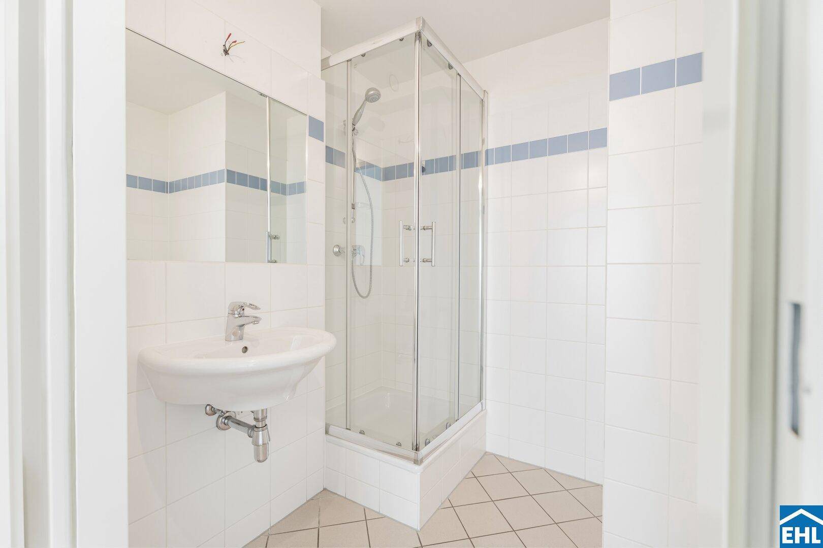 Badezimmer mit Duschkabine, Waschbecken und weißen Fliesen.