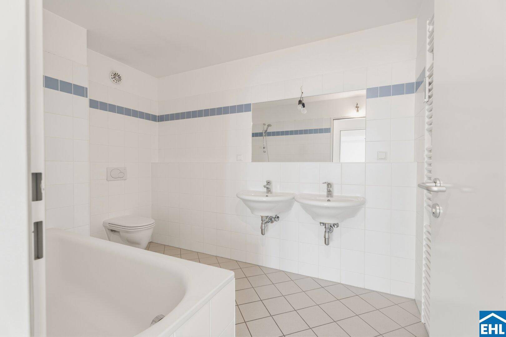 Badezimmer mit Badewanne, Doppelwaschbecken und Wand-WC.