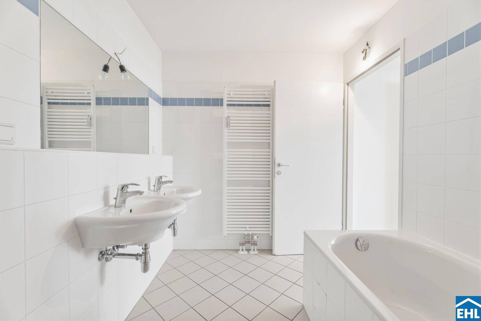 Helles Badezimmer mit Badewanne, Doppelwaschbecken und Handtuchheizkörper.
