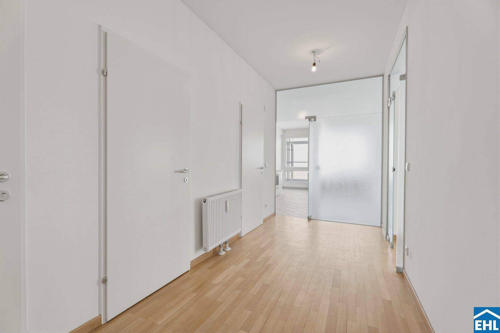 Heller Flur mit Parkettboden und einer modernen Glastür.