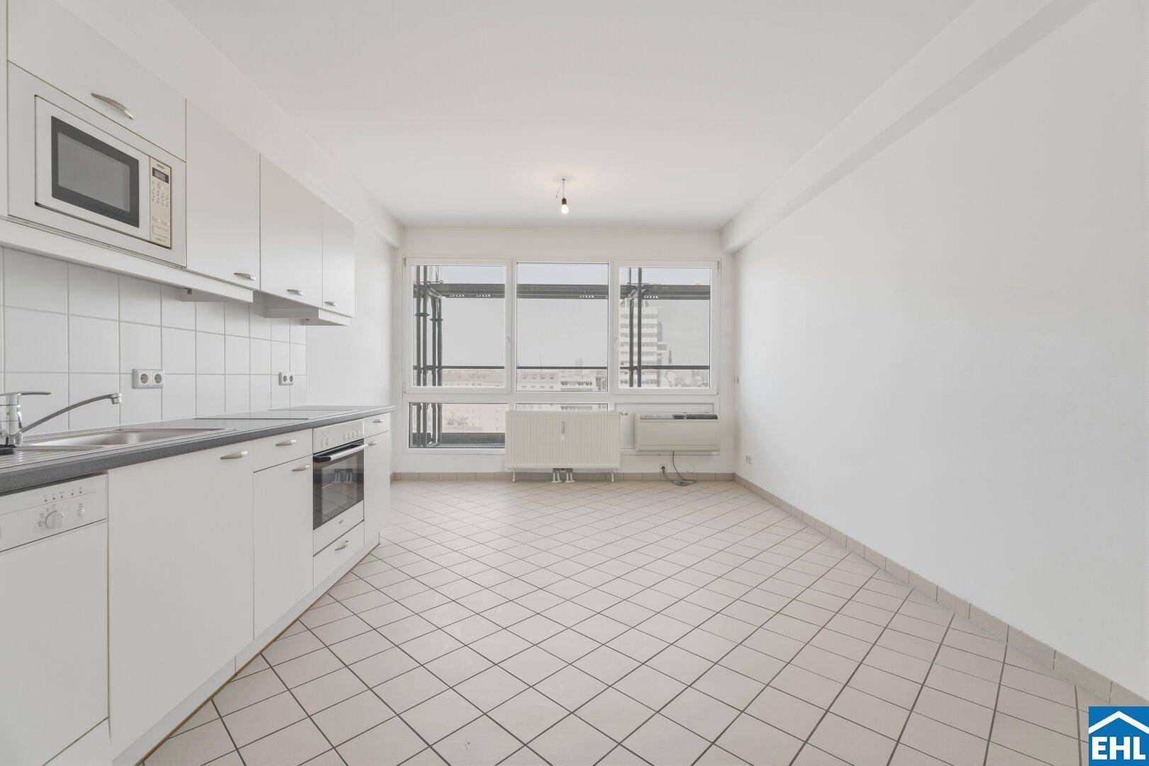 Leerer Küchenbereich mit Fliesenboden und großer Fensterfront.