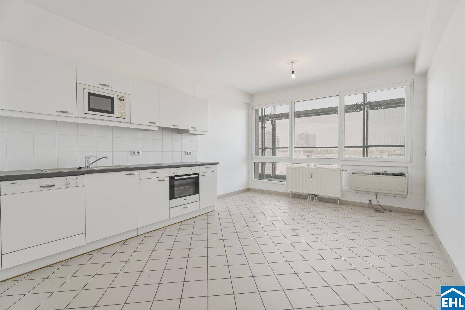 Leerer Küchenbereich mit Fliesenboden und breiter Fensterfront.