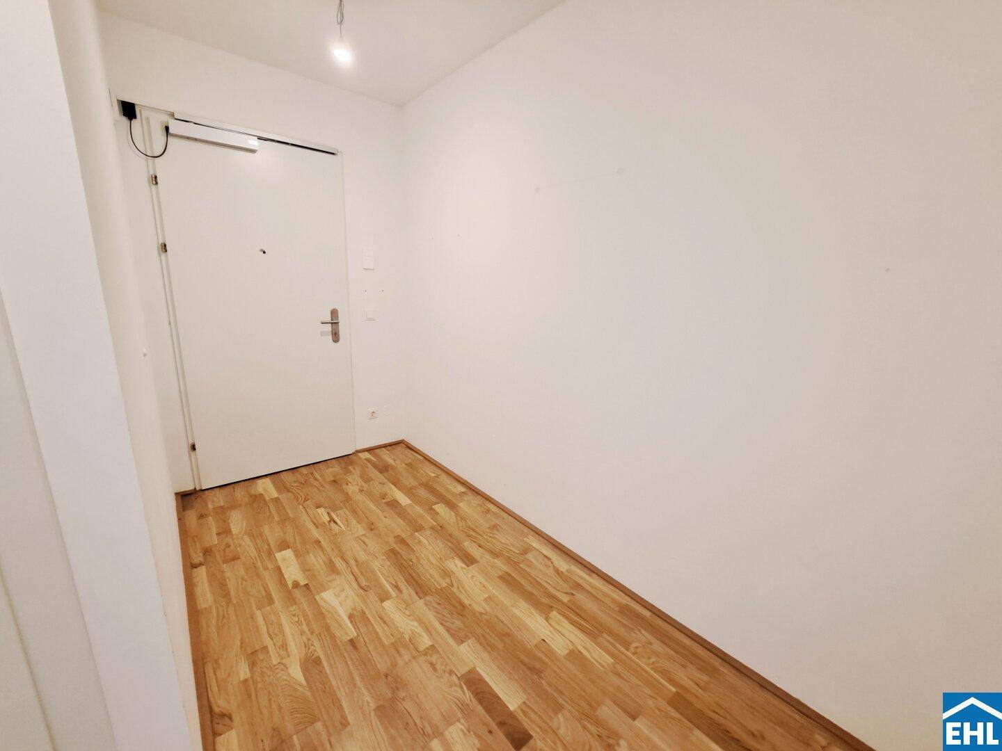 Heller Eingangsbereich mit Parkettboden und weißer Tür, die in die Wohnung führt.
