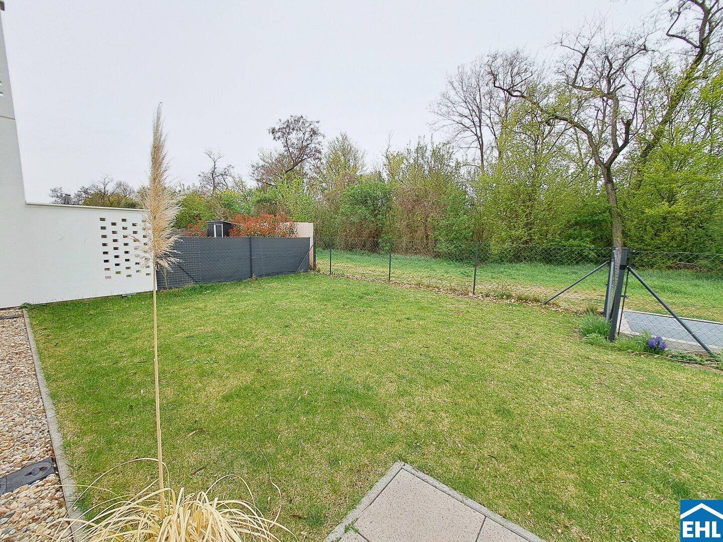 Großer Gartenbereich mit Rasenfläche und Bäumen im Hintergrund, ideal zum Entspannen.