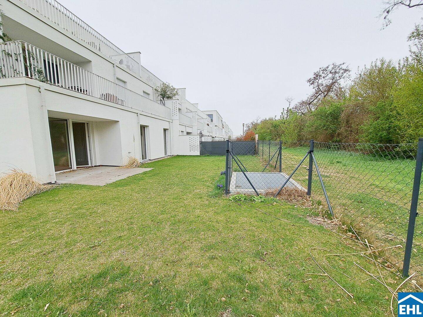 Gepflegter Rasenbereich hinter dem Gebäude mit angrenzender Terrasse und Zaun.