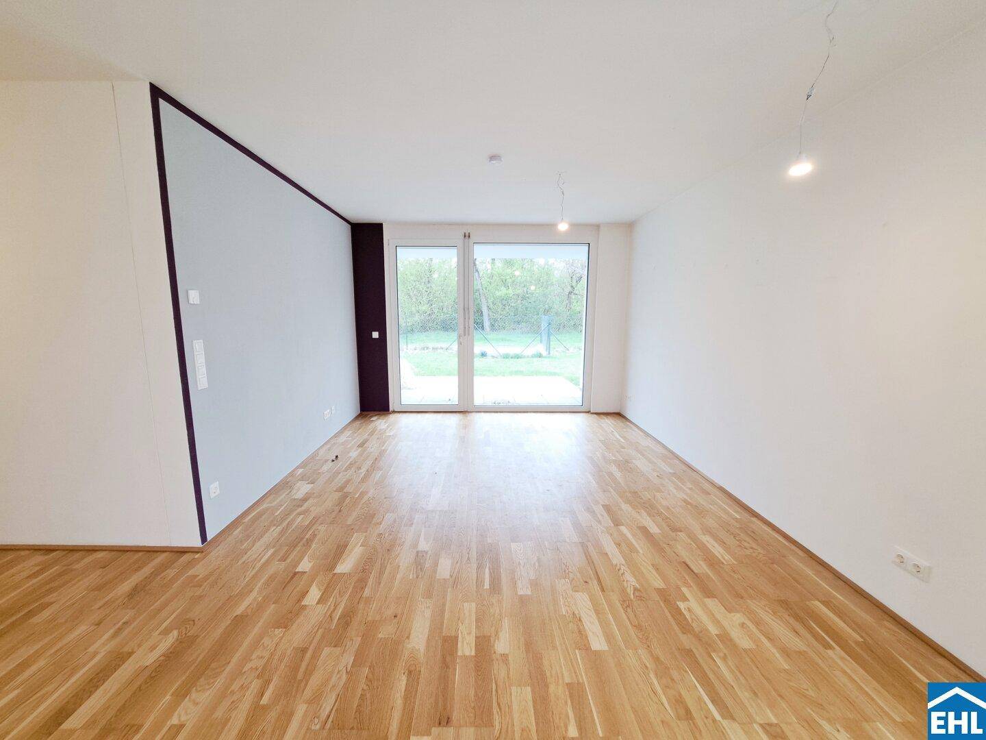 Heller Wohnraum mit großen Fenstern und direktem Zugang zum grünen Außenbereich.