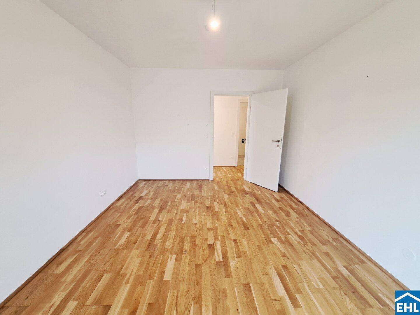 Helles, leeres Zimmer mit Parkettboden und weiß gestrichenen Wänden, bereit zur Einrichtung.