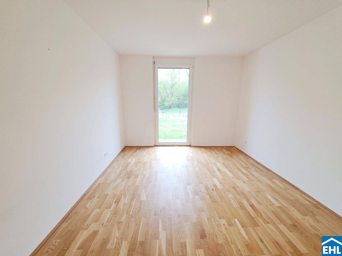 Leeres Schlafzimmer mit Parkettboden und Zugang zu einem Außenbereich durch eine Glastür.