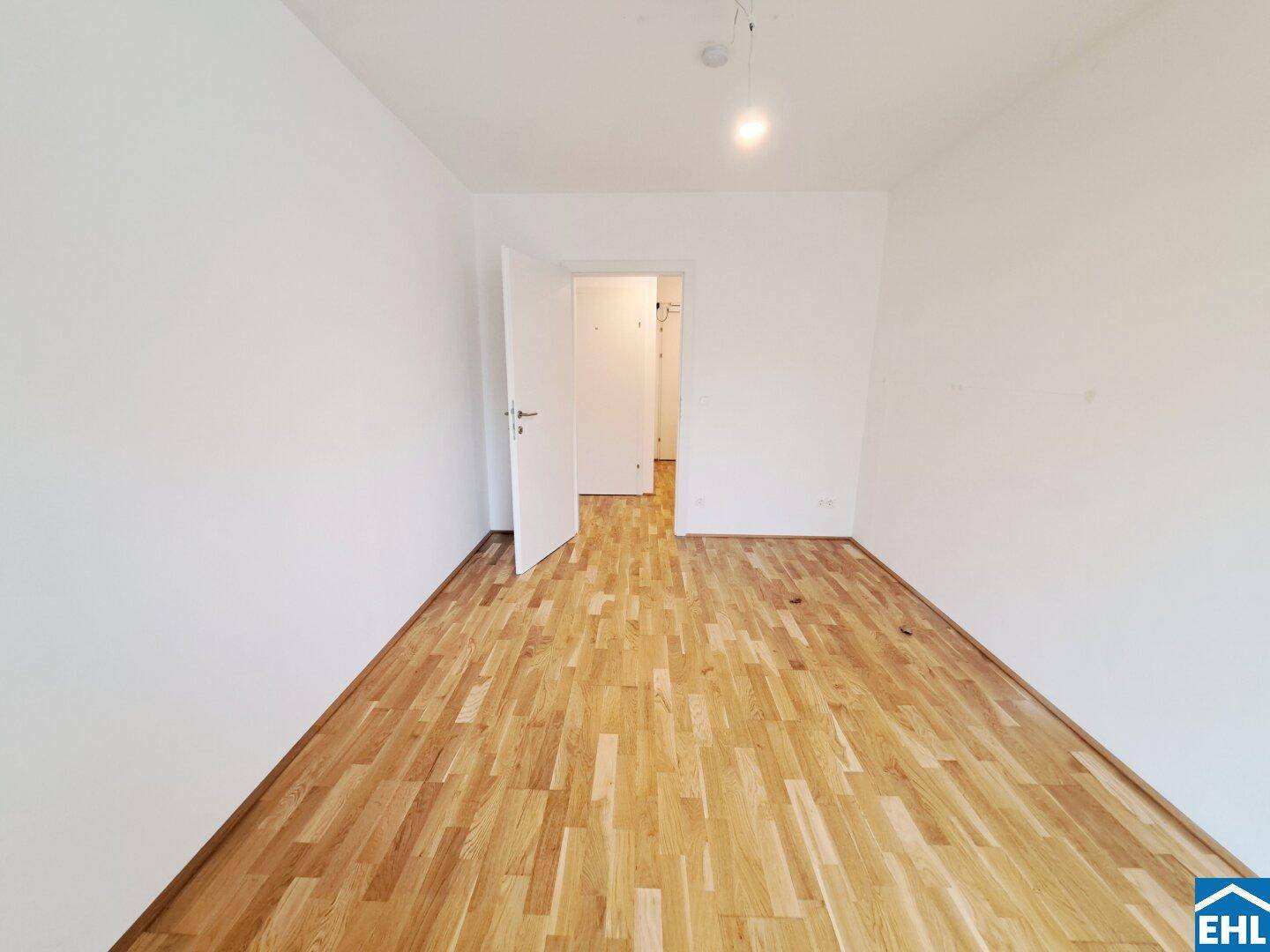 Unmöbliertes Zimmer mit Holzboden und weiß gestrichenen Wänden, ideal als Schlafzimmer.