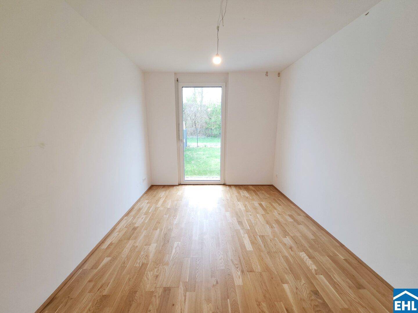Helles Zimmer mit Parkettboden und einer Glastür, die den Blick ins Grüne freigibt.
