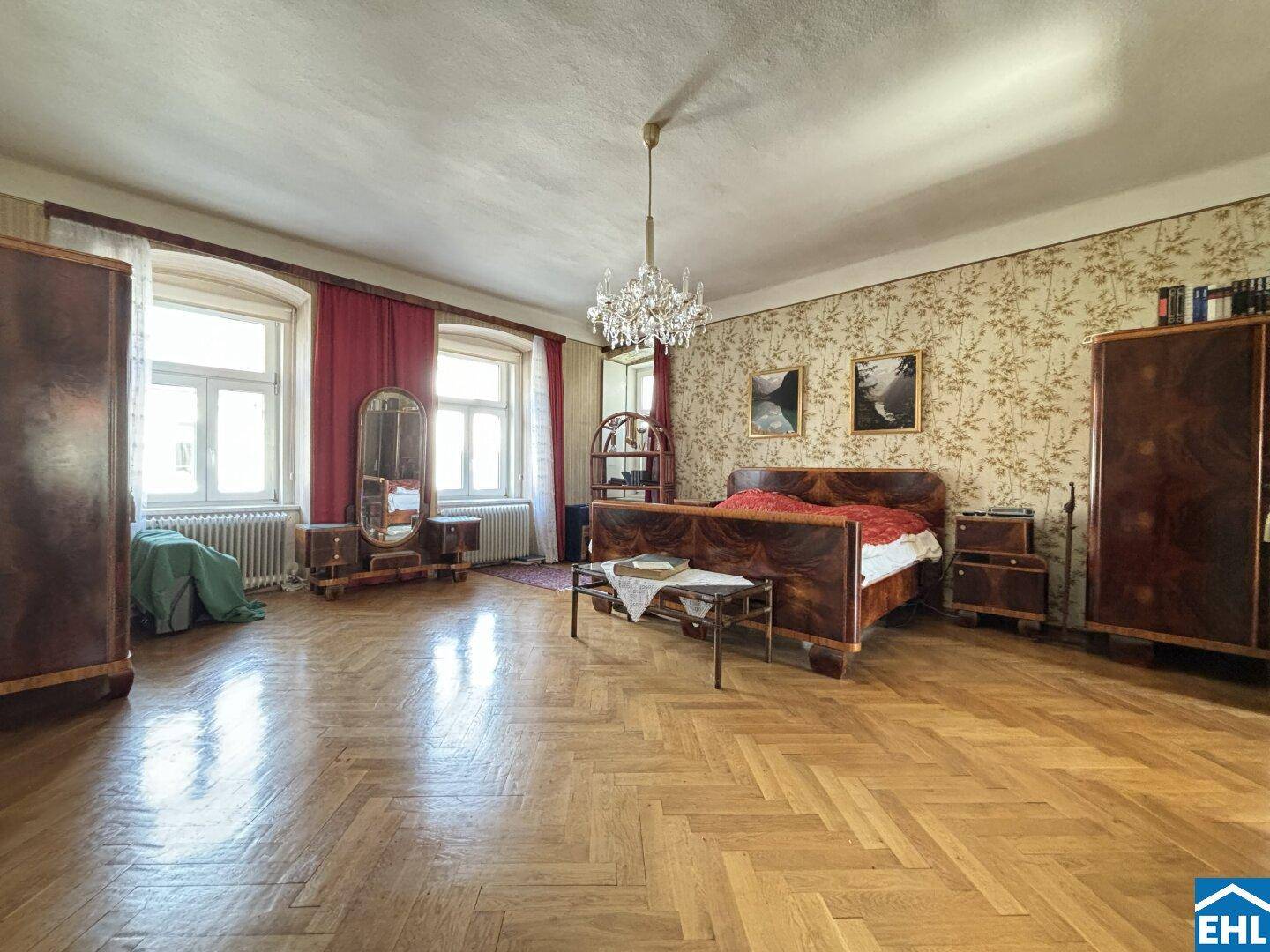Großes Schlafzimmer mit Fischgrätparkett, floraler Tapete und antiken Möbeln in einem Altbau.