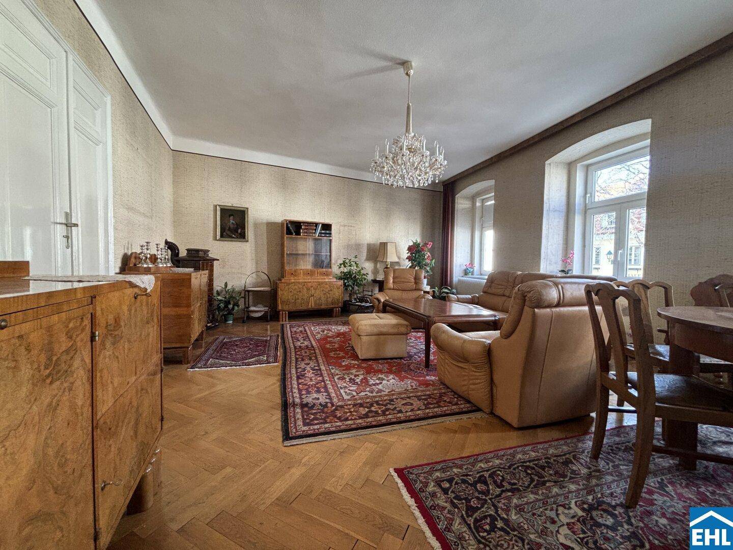 Geräumiges Wohnzimmer mit Fischgrätparkett, Kronleuchter und traditionellen Möbeln in einem Altbau.