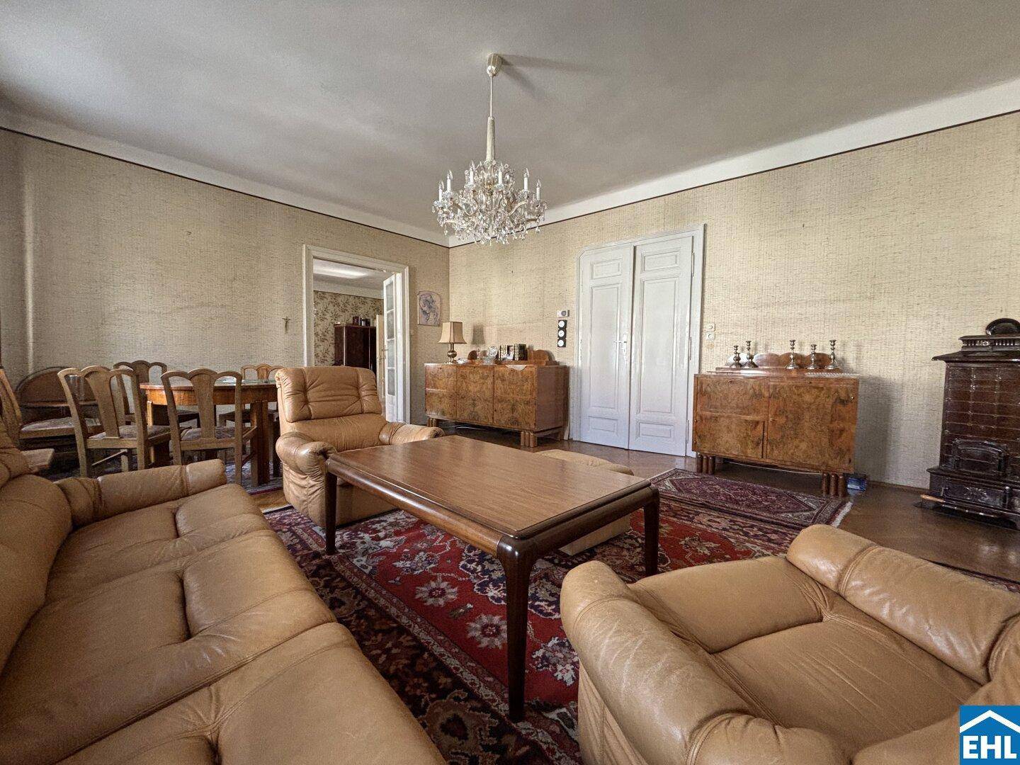 Klassisches Wohnzimmer mit Ledersofas, Kronleuchter und einem traditionellen Kachelofen in einem Altbau.