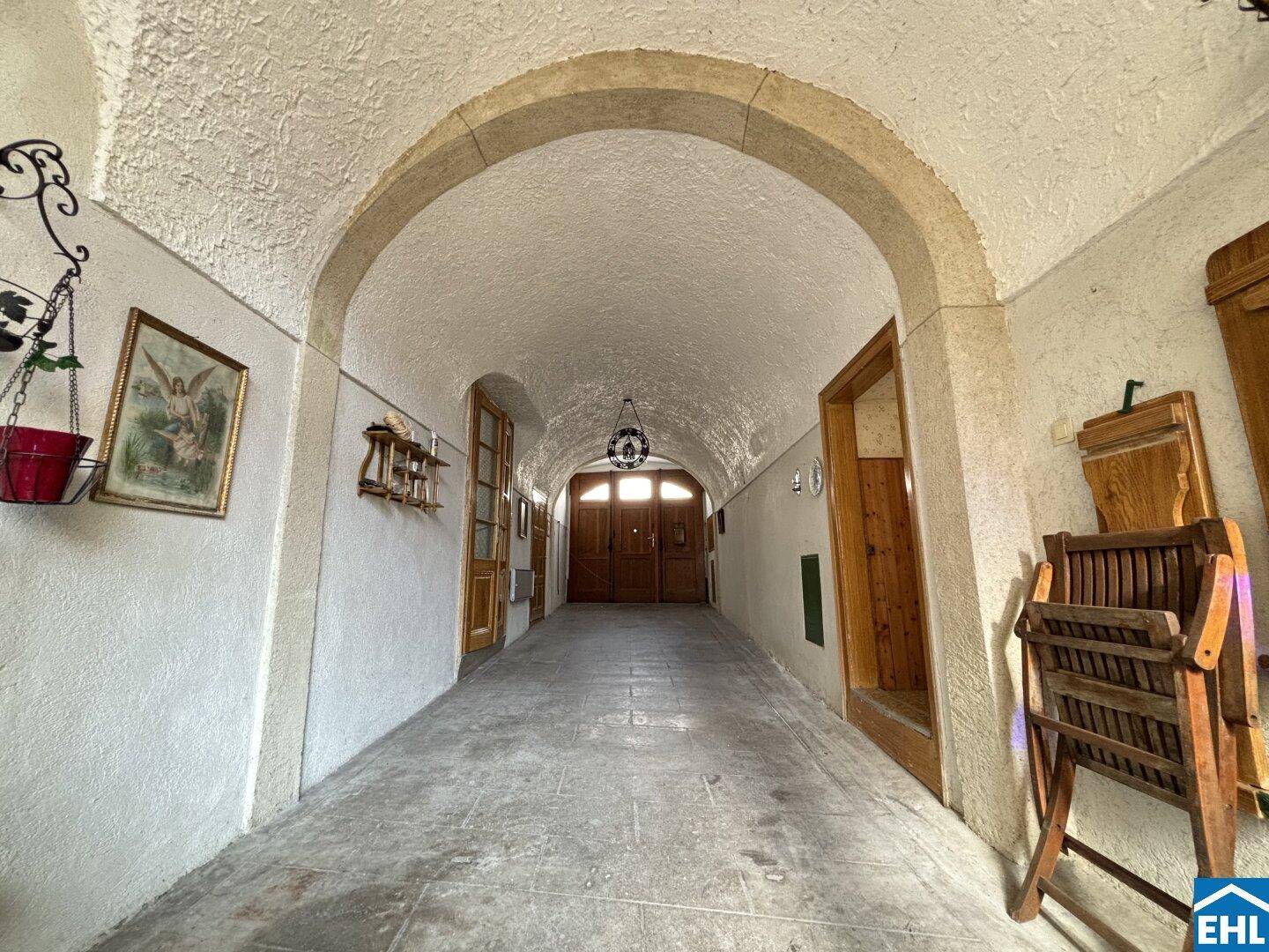 Historischer Eingangsbereich mit Gewölbedecke, Steinboden und massiven Holztüren in einem Altbau.