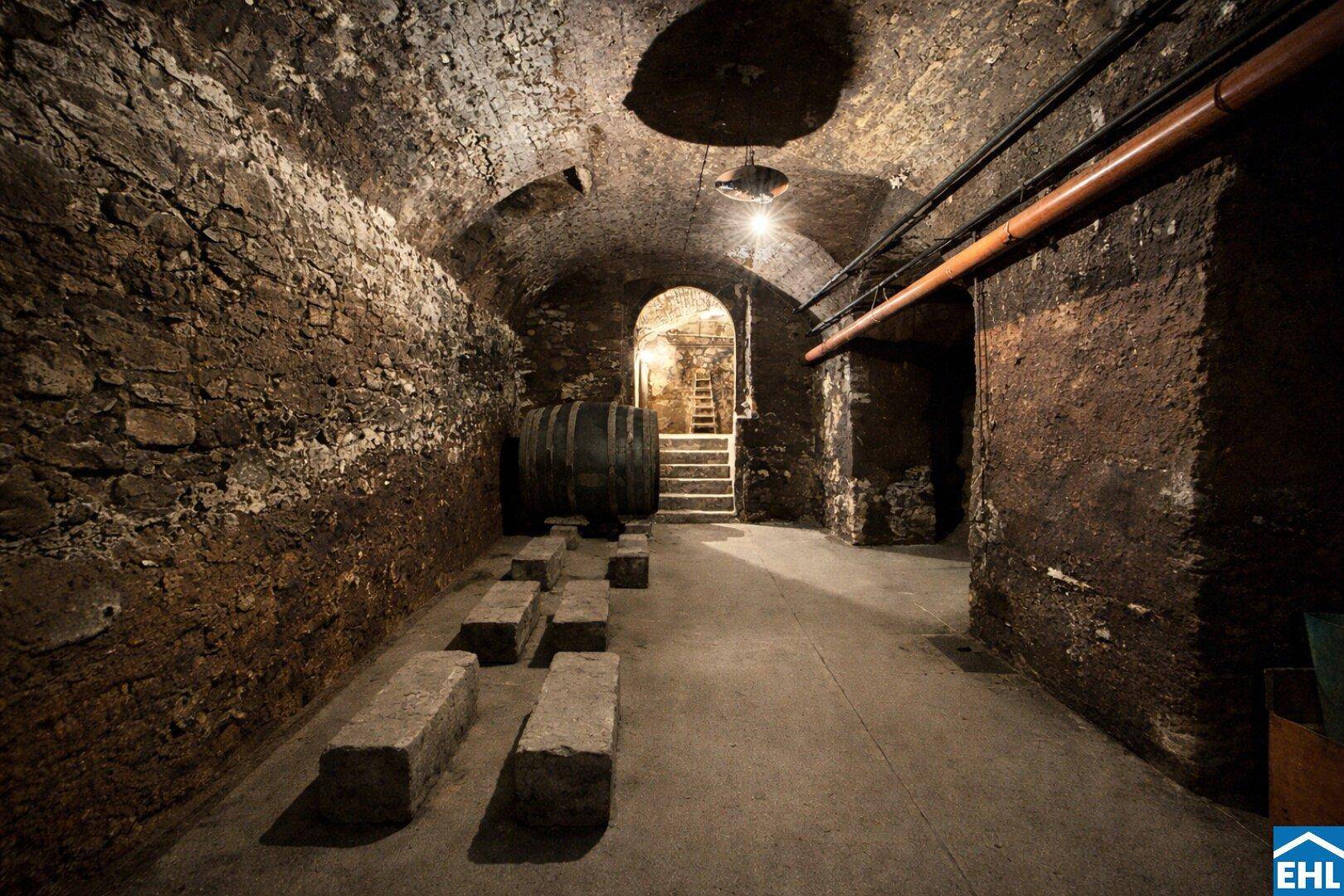 Historischer Weinkeller mit groben Steinmauern, Gewölbedecke und alten Holzfässern.