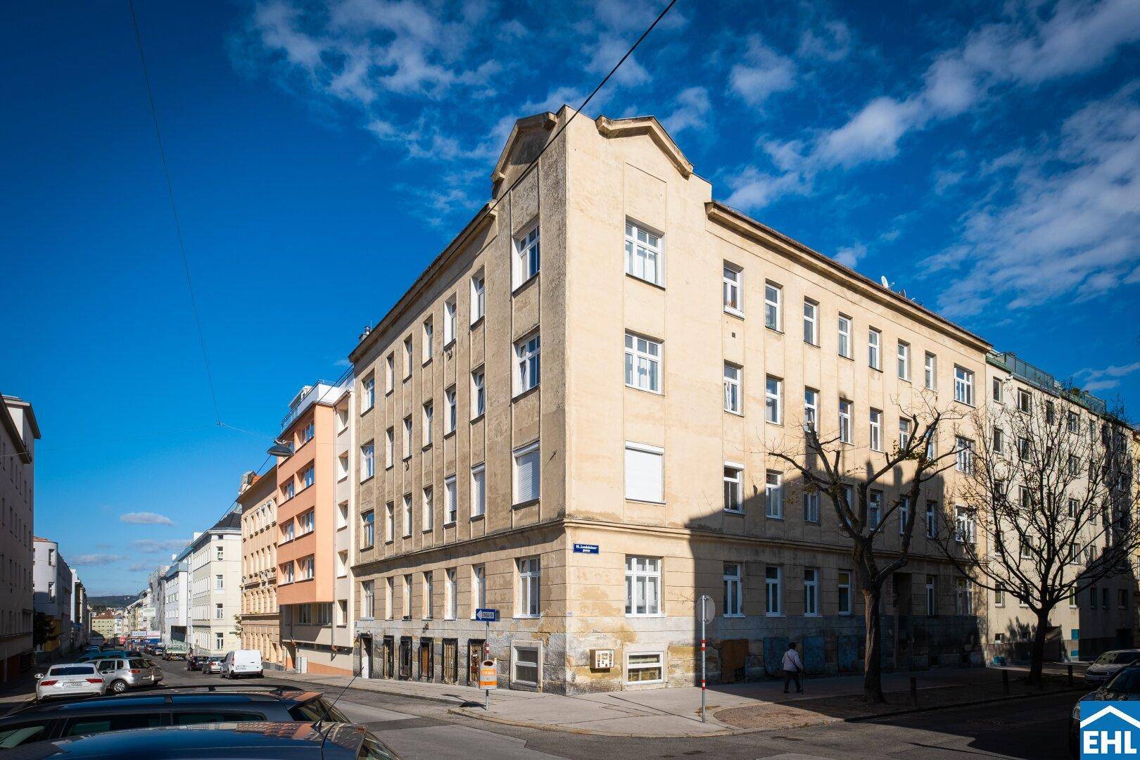 Eckansicht eines älteren Mehrfamilienhauses mit vielen Fenstern an einer Stadtstraße.