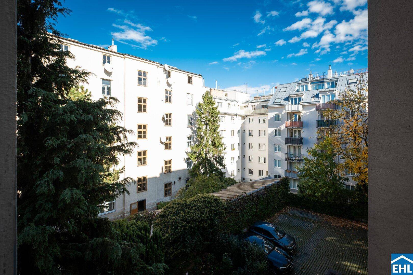 Innenhof mit Bäumen und Parkplätzen, umgeben von Wohngebäuden unter blauem Himmel.