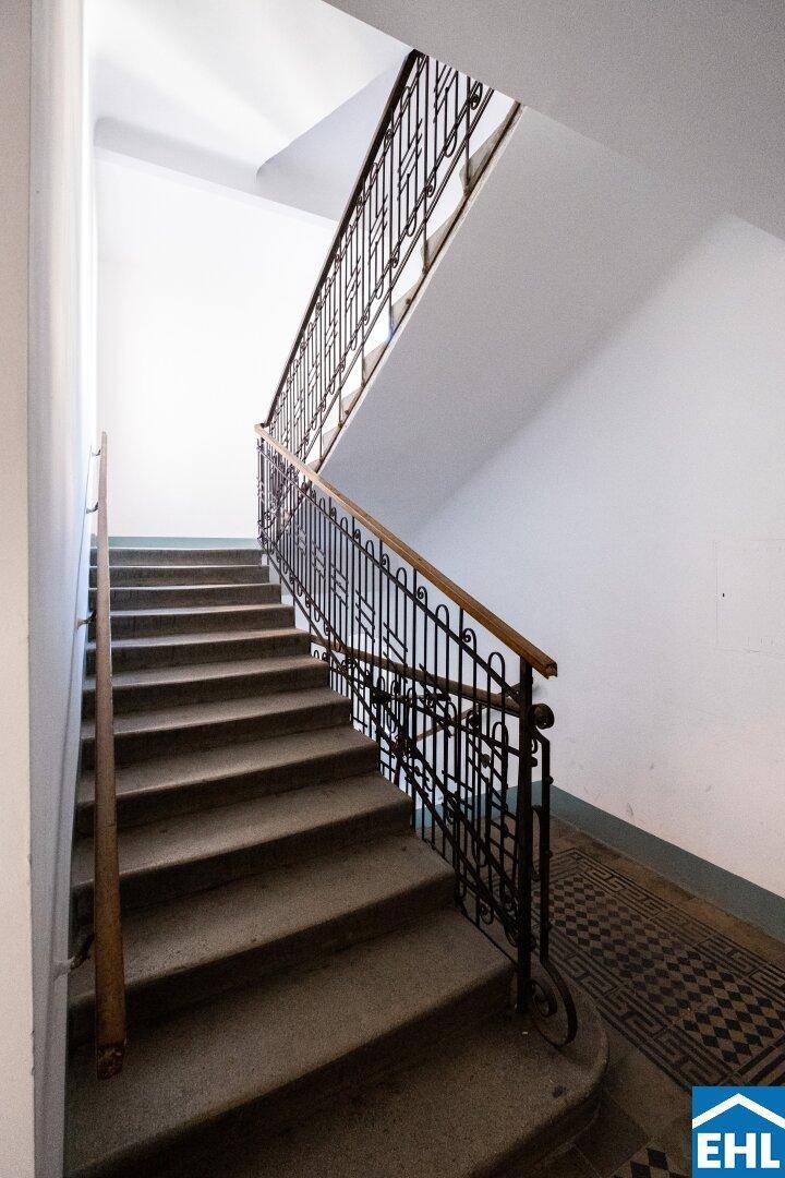 Klassisches Treppenhaus mit schmiedeeisernem Geländer und Steinstufen in einem Altbau.