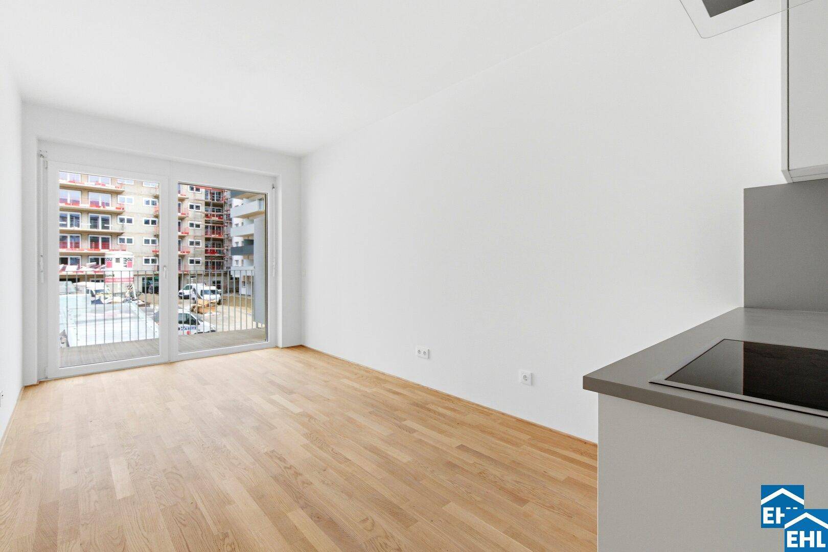 Heller Wohnbereich mit großem Fenster und Zugang zu einem Balkon, Blick auf Neubauten.