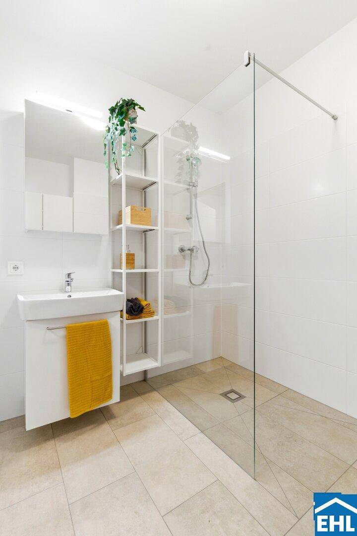 Modernes Badezimmer mit ebenerdiger Dusche, Waschbecken und weißen Fliesen.