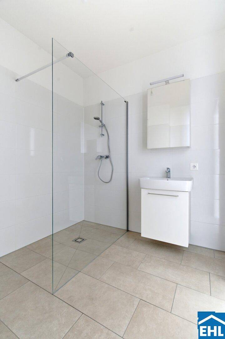 Helles Badezimmer mit großer ebenerdiger Dusche und modernem Waschbecken.