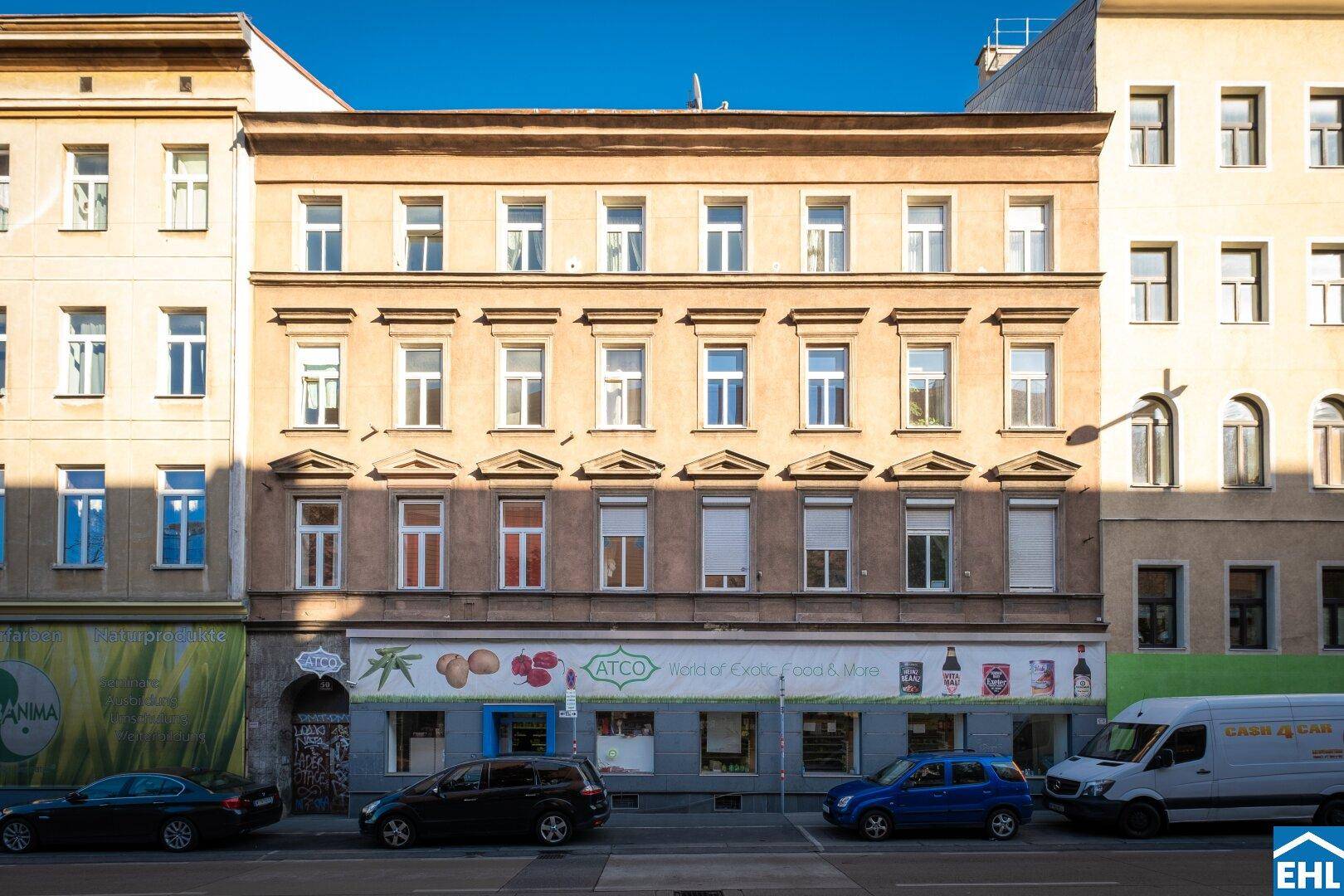Historische Fassade eines Mehrfamilienhauses mit vielen Fenstern und Geschäften im Erdgeschoss.