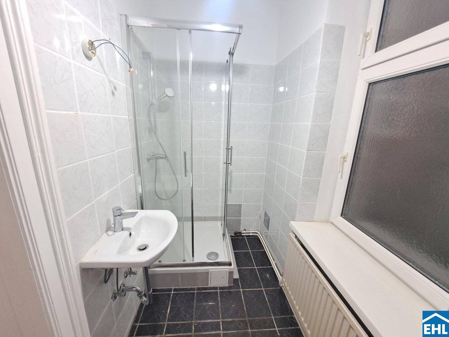 Kleines Badezimmer mit Duschkabine, Waschbecken und weißen Fliesen, ausgestattet mit einem Fenster.