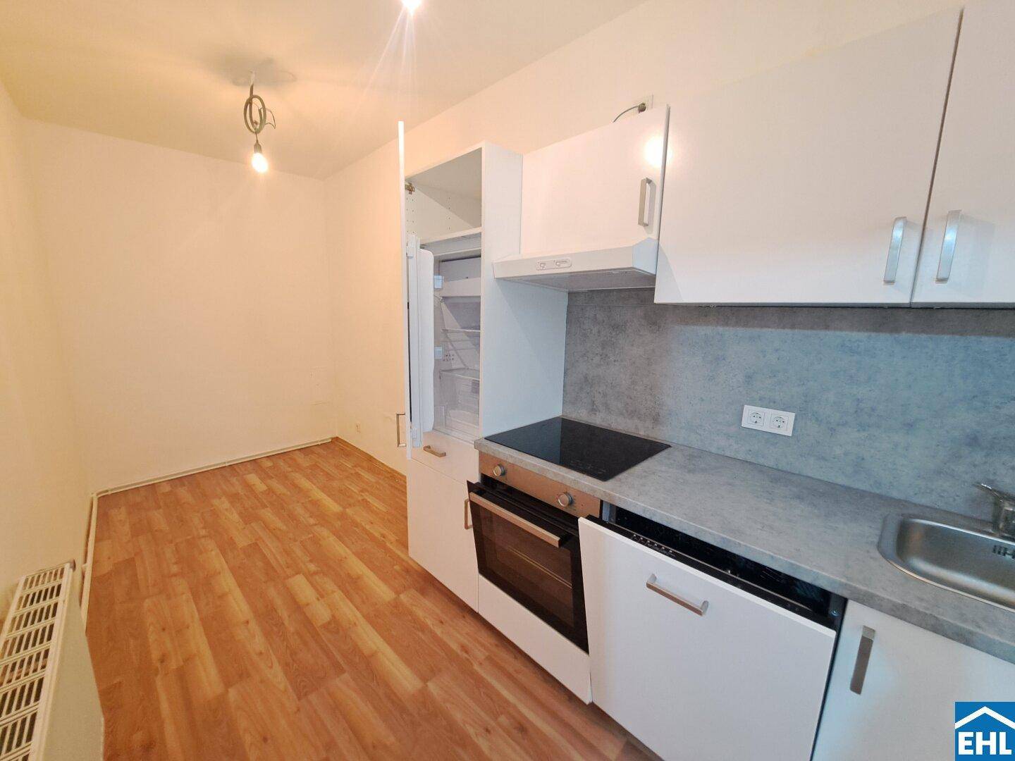 Kleine, moderne Küchenzeile mit weißen Schränken, Kochfeld und integriertem Kühlschrank.