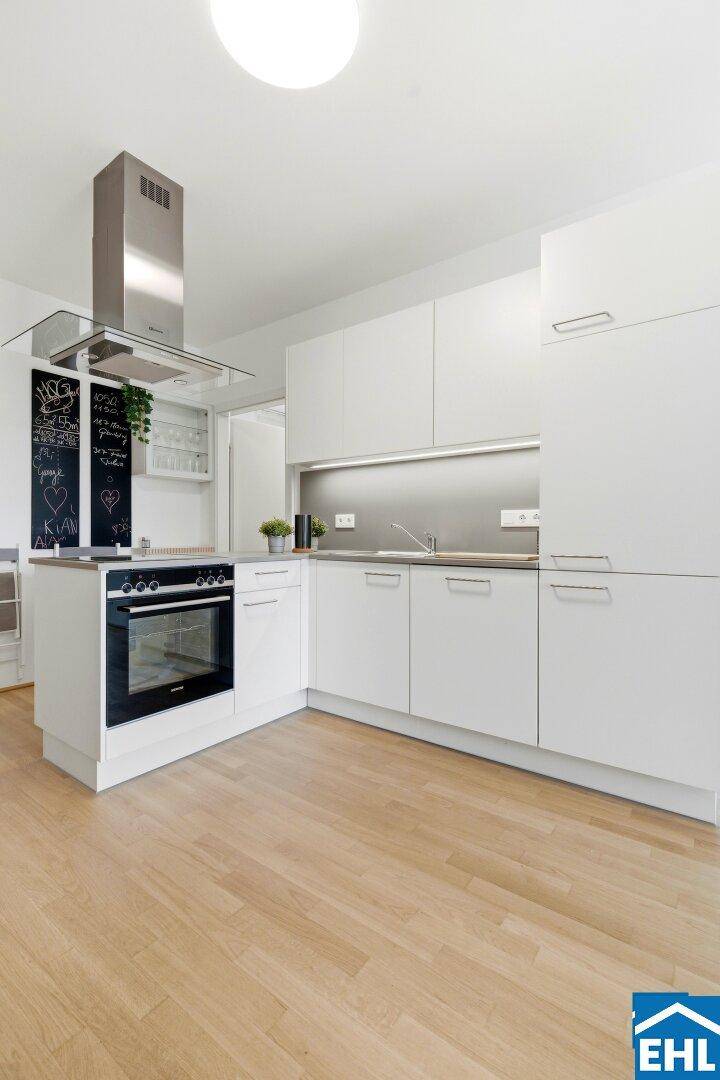 Helle Küche mit weißen Schränken, integriertem Backofen und Edelstahl-Dunstabzugshaube.