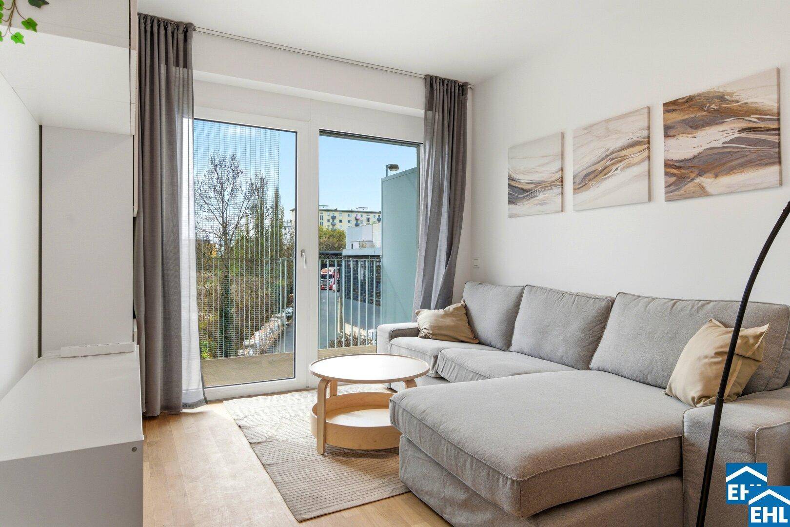 Heller Wohnbereich mit bequemer Couch, Holzboden und direktem Zugang zu einem Balkon.